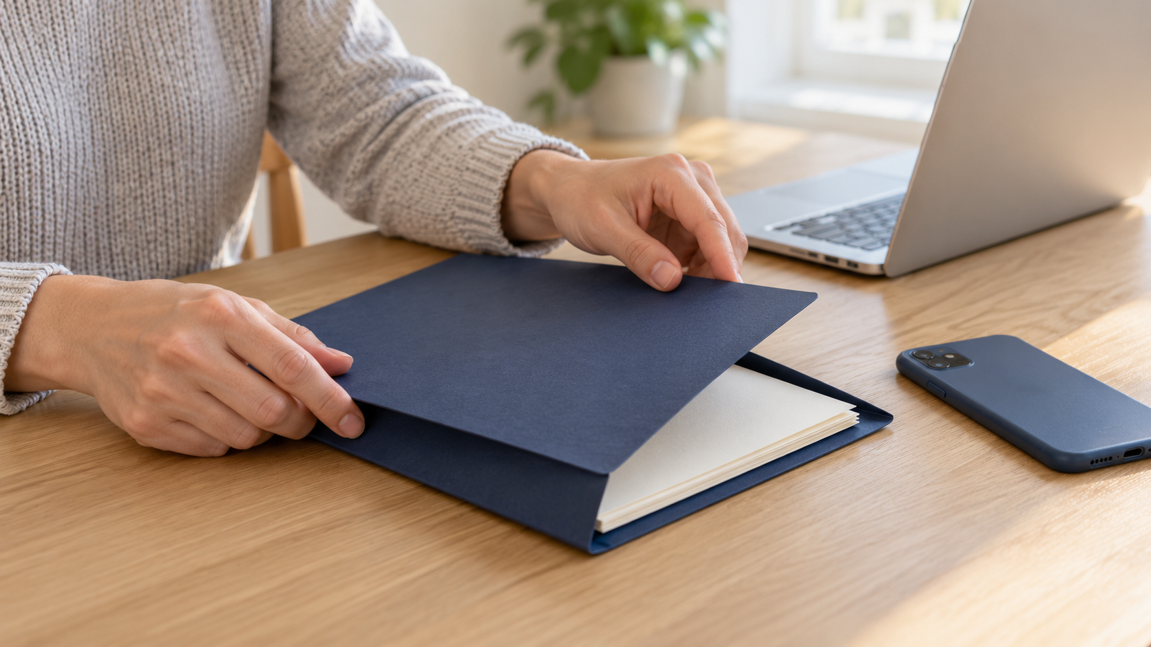 Hands closing a plain document folder beside a laptop and a face-down phone